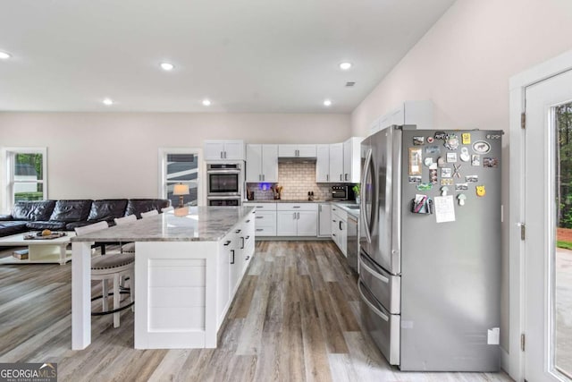 kitchen featuring stainless steel appliances, white cabinets, light stone counters, light wood-type flooring, and a center island