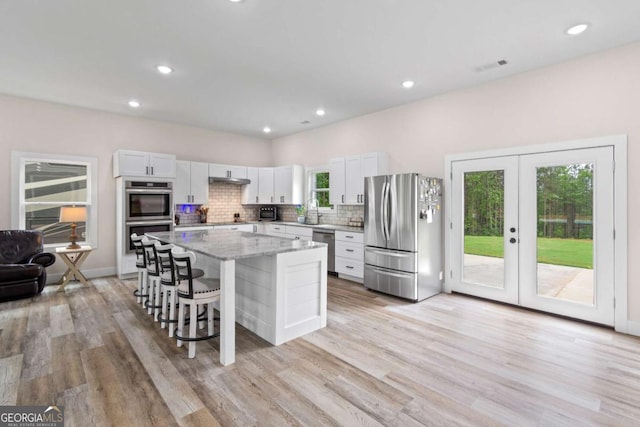 kitchen with appliances with stainless steel finishes, a breakfast bar area, light wood finished floors, a center island, and tasteful backsplash