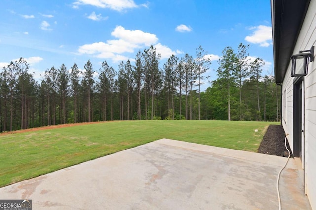 view of grassy yard featuring a patio and a view of trees