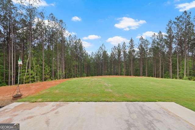 view of green lawn with a forest view