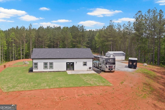 back of property featuring a view of trees, a lawn, and dirt driveway