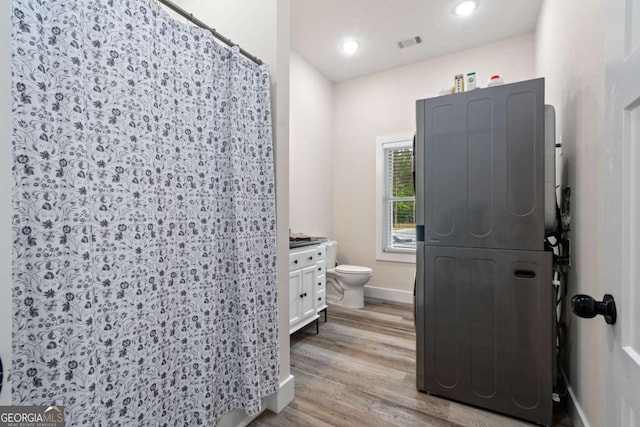 full bathroom featuring stacked washer and clothes dryer, wood finished floors, toilet, baseboards, and vanity