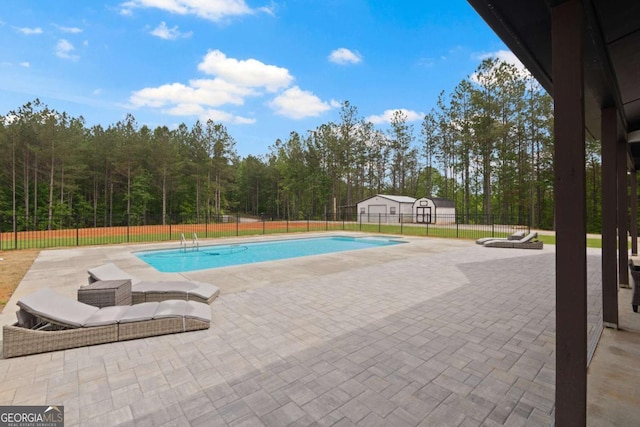 view of pool with a patio area, fence, an outbuilding, and a forest view