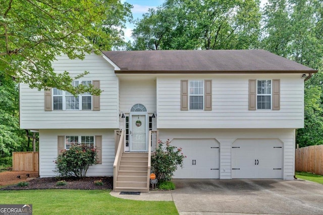 raised ranch featuring fence, an attached garage, concrete driveway, and a shingled roof