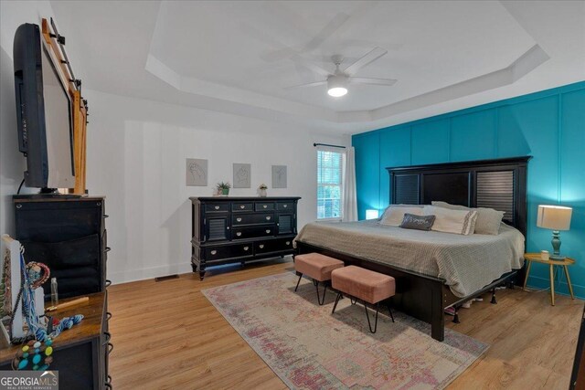 bedroom with a raised ceiling, light wood-type flooring, a ceiling fan, and baseboards