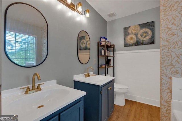 bathroom with wood finished floors, two vanities, and toilet