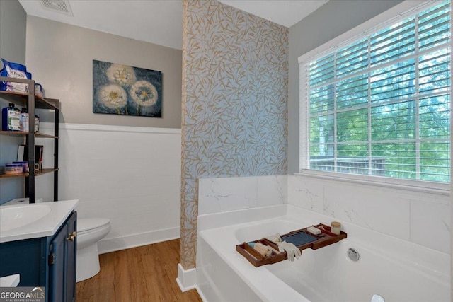 full bathroom featuring wood finished floors, a bath, wainscoting, toilet, and vanity