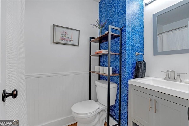 bathroom featuring toilet, vanity, and a wainscoted wall