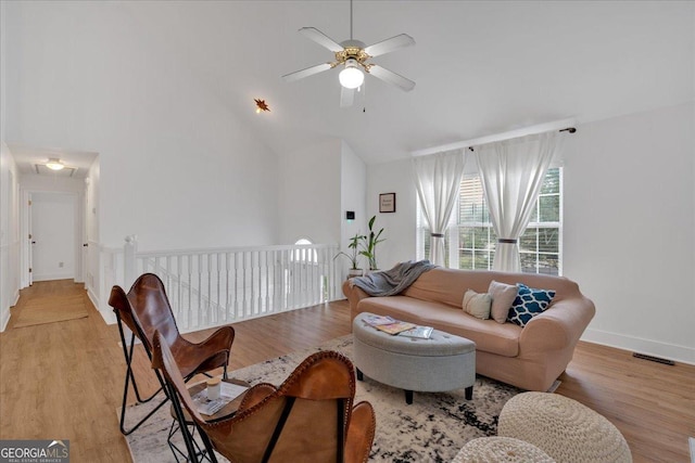living room featuring high vaulted ceiling, a ceiling fan, light wood finished floors, attic access, and baseboards