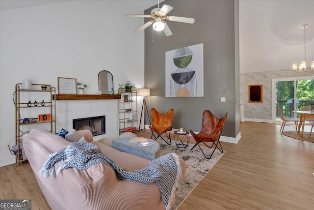 living room featuring a towering ceiling, baseboards, a tiled fireplace, wood finished floors, and a chandelier