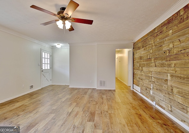 empty room with light wood-style floors, a ceiling fan, ornamental molding, wood walls, and a textured ceiling