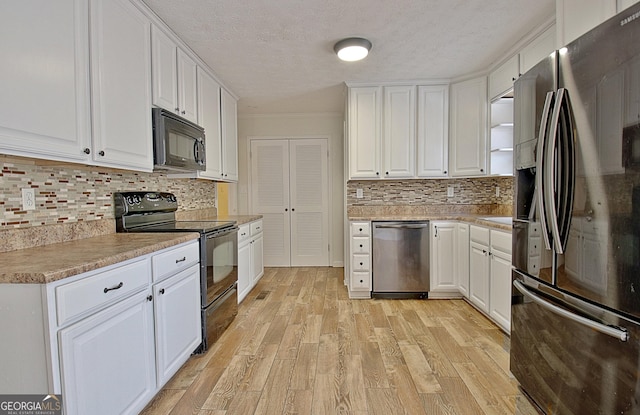 kitchen with black appliances, a textured ceiling, white cabinets, decorative backsplash, and light wood-style floors