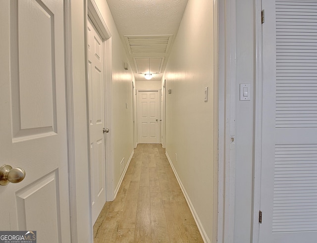 hallway featuring attic access, light wood-style flooring, and baseboards