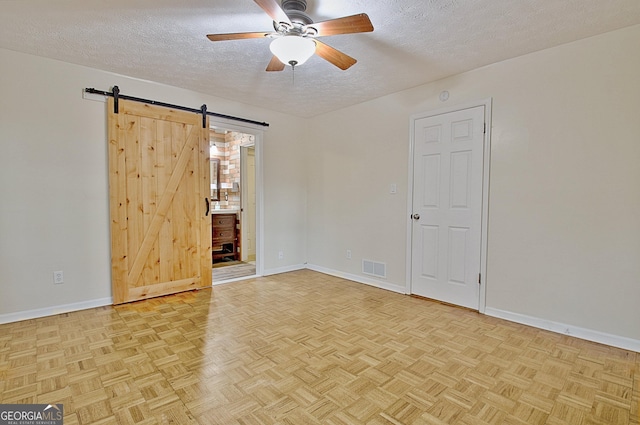 spare room with a textured ceiling, a barn door, a ceiling fan, and baseboards