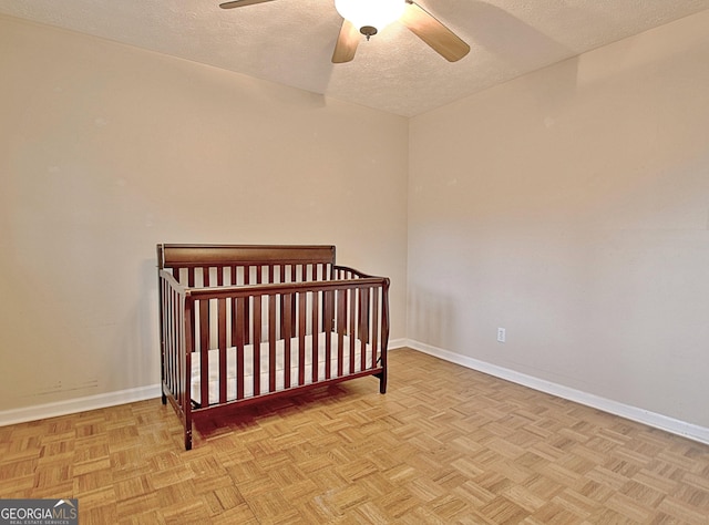 bedroom with a textured ceiling, baseboards, a crib, and a ceiling fan