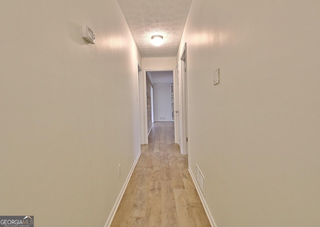 hallway with a textured ceiling, light wood-type flooring, and baseboards