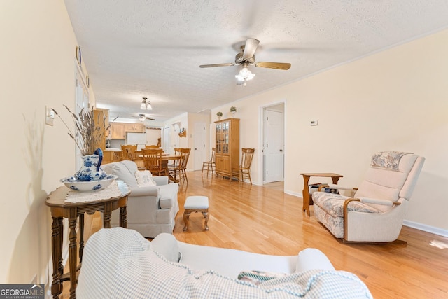 living area featuring ceiling fan, a textured ceiling, light wood-type flooring, baseboards, and ornamental molding
