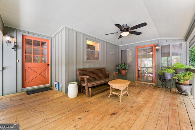 entrance to property with a ceiling fan, board and batten siding, and a deck