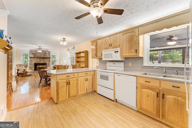kitchen featuring white appliances, ceiling fan, a peninsula, a stone fireplace, and light wood-style floors