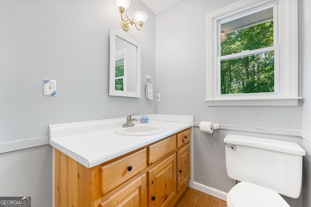 half bathroom with toilet, baseboards, vanity, and wood finished floors