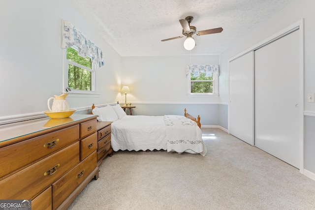 bedroom with multiple windows, a closet, light carpet, a textured ceiling, and ceiling fan
