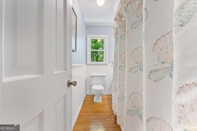 bathroom with toilet, wood finished floors, baseboards, and a textured ceiling
