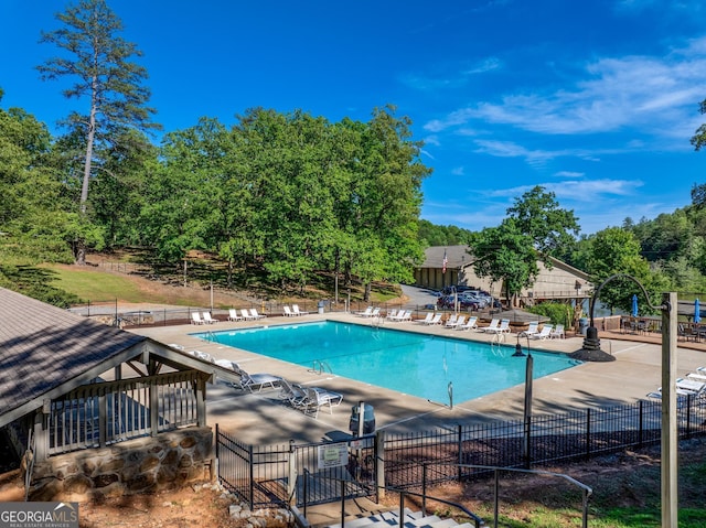 community pool with fence, a patio area, and view of wooded area