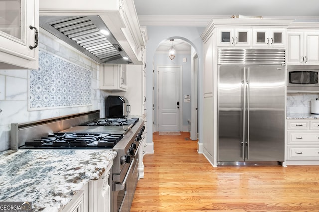 8340 Colonial Pl, Duluth, GA 30097 - kitchen featuring built in appliances, premium range hood, white cabinets, ornamental molding, and arched walkways