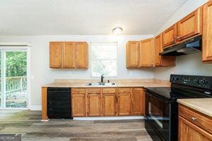 kitchen featuring black appliances, under cabinet range hood, a sink, light countertops, and wood finished floors