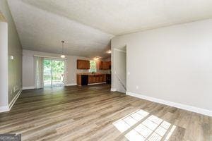 unfurnished living room featuring wood finished floors, vaulted ceiling, and baseboards