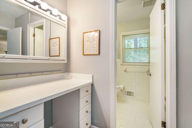bathroom with vanity, toilet, tile patterned flooring, and tile walls