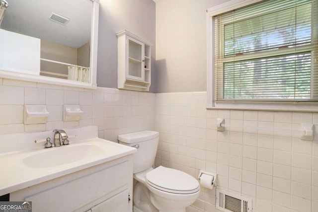 bathroom featuring tile walls, toilet, vanity, a shower with shower curtain, and wainscoting