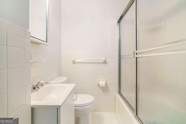 full bathroom featuring tile walls, toilet, vanity, shower / bath combination with glass door, and tile patterned floors