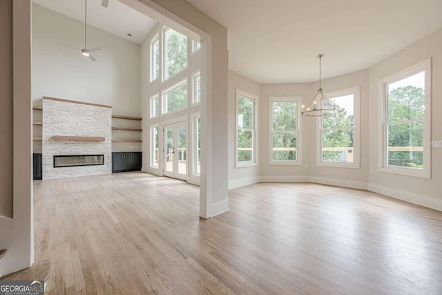 2555 Chattahoochee Ln, Cumming, GA 30041 - unfurnished living room with a stone fireplace, light wood-type flooring, healthy amount of natural light, a chandelier, and a towering ceiling