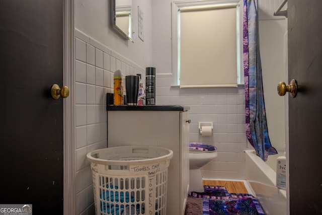 bathroom featuring tile walls, wood finished floors, wainscoting, shower / bathtub combination with curtain, and toilet