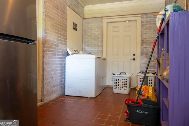 laundry room featuring brick wall, separate washer and dryer, and dark tile patterned flooring