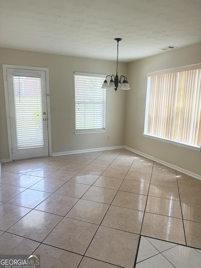 unfurnished dining area with light tile patterned flooring, a chandelier, baseboards, and a textured ceiling
