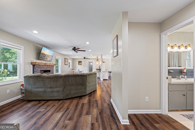 living area with dark wood-type flooring, a brick fireplace, a ceiling fan, recessed lighting, and baseboards