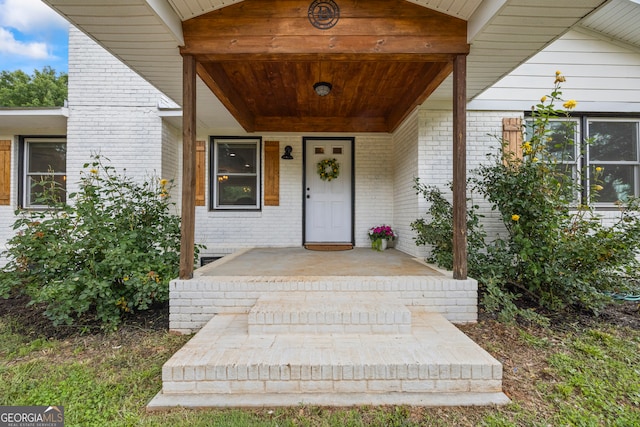 view of exterior entry featuring brick siding and a porch