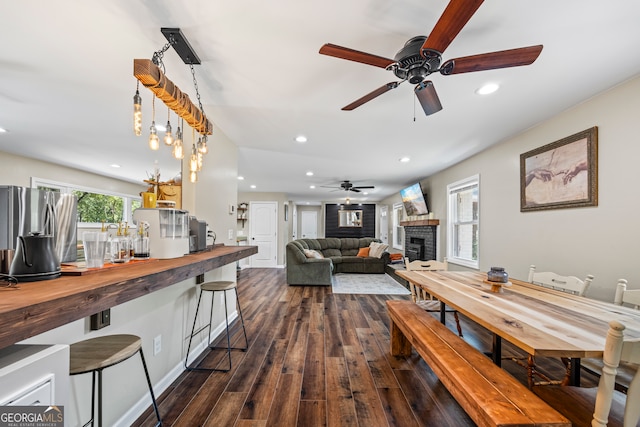dining room featuring a ceiling fan, dark wood finished floors, recessed lighting, and a brick fireplace