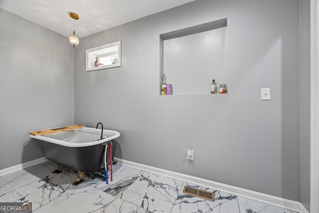 bathroom with marble look tile flooring, a freestanding bath, and baseboards