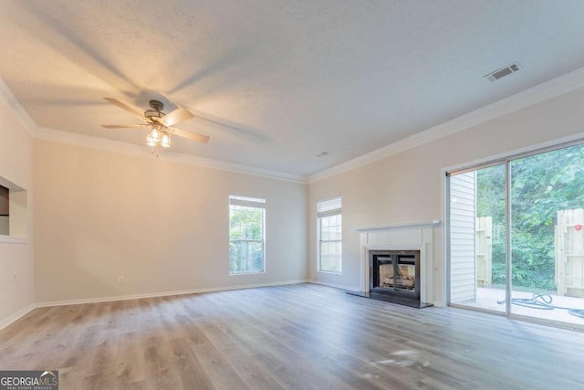 unfurnished living room with light wood-type flooring, ornamental molding, plenty of natural light, a fireplace with raised hearth, and a ceiling fan