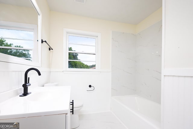 full bath with marble finish floors, toilet, vanity, a wainscoted wall, and washtub / shower combination