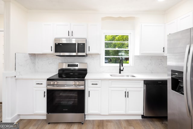kitchen featuring appliances with stainless steel finishes, a sink, white cabinets, light countertops, and tasteful backsplash