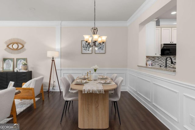 dining area featuring ornamental molding, a chandelier, dark wood finished floors, wainscoting, and a decorative wall