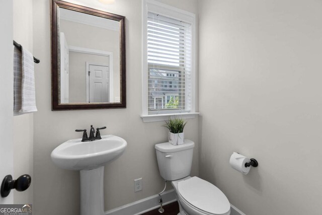 half bathroom with baseboards, toilet, and a sink