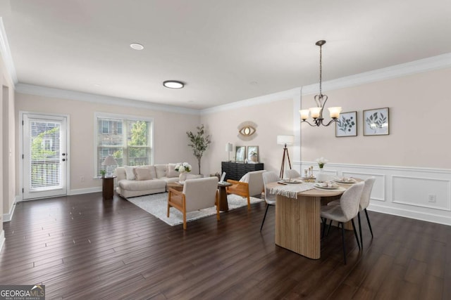 dining area with dark wood-type flooring, ornamental molding, a chandelier, and wainscoting