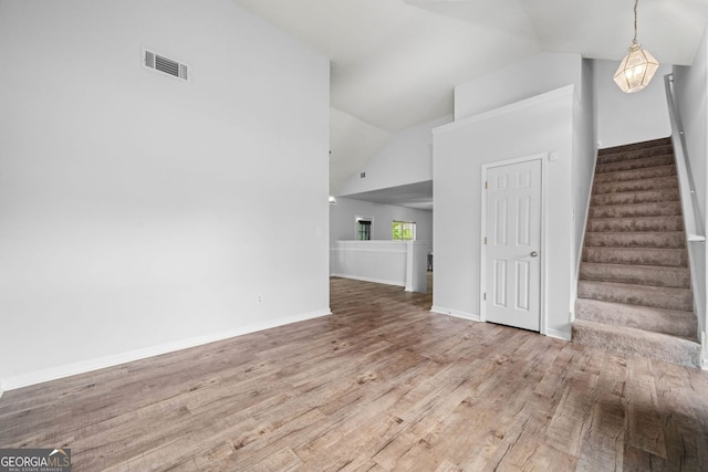 unfurnished living room with wood finished floors, stairway, baseboards, and high vaulted ceiling