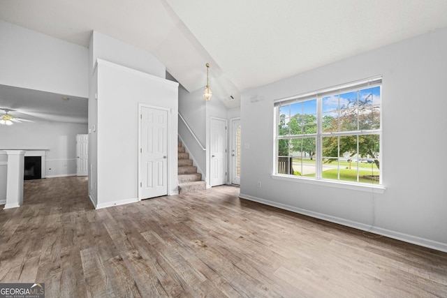 unfurnished living room featuring wood finished floors, lofted ceiling, stairway, a fireplace, and baseboards