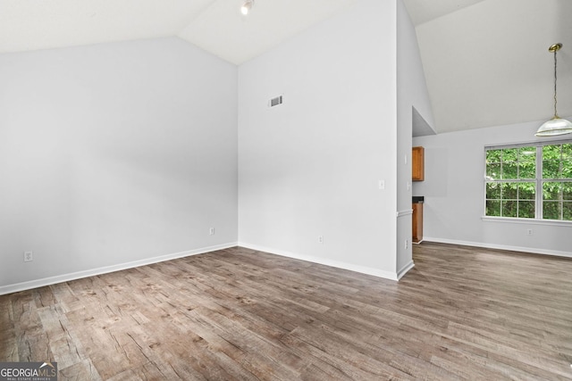 empty room featuring wood finished floors, high vaulted ceiling, and baseboards